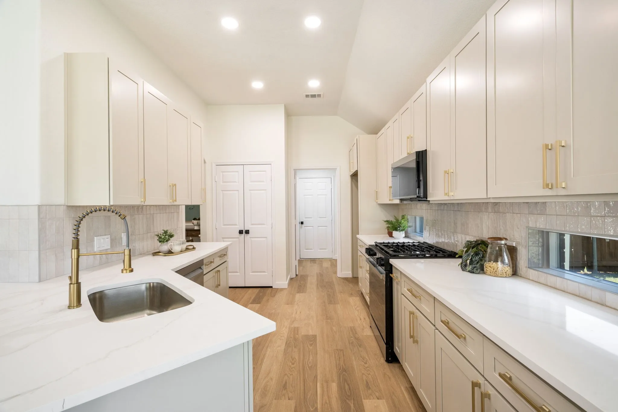 Kitchen with wood-finish flooring, recessed lighting, white cabinetry, a gold-tone pull-down faucet, and a stainless steel sink