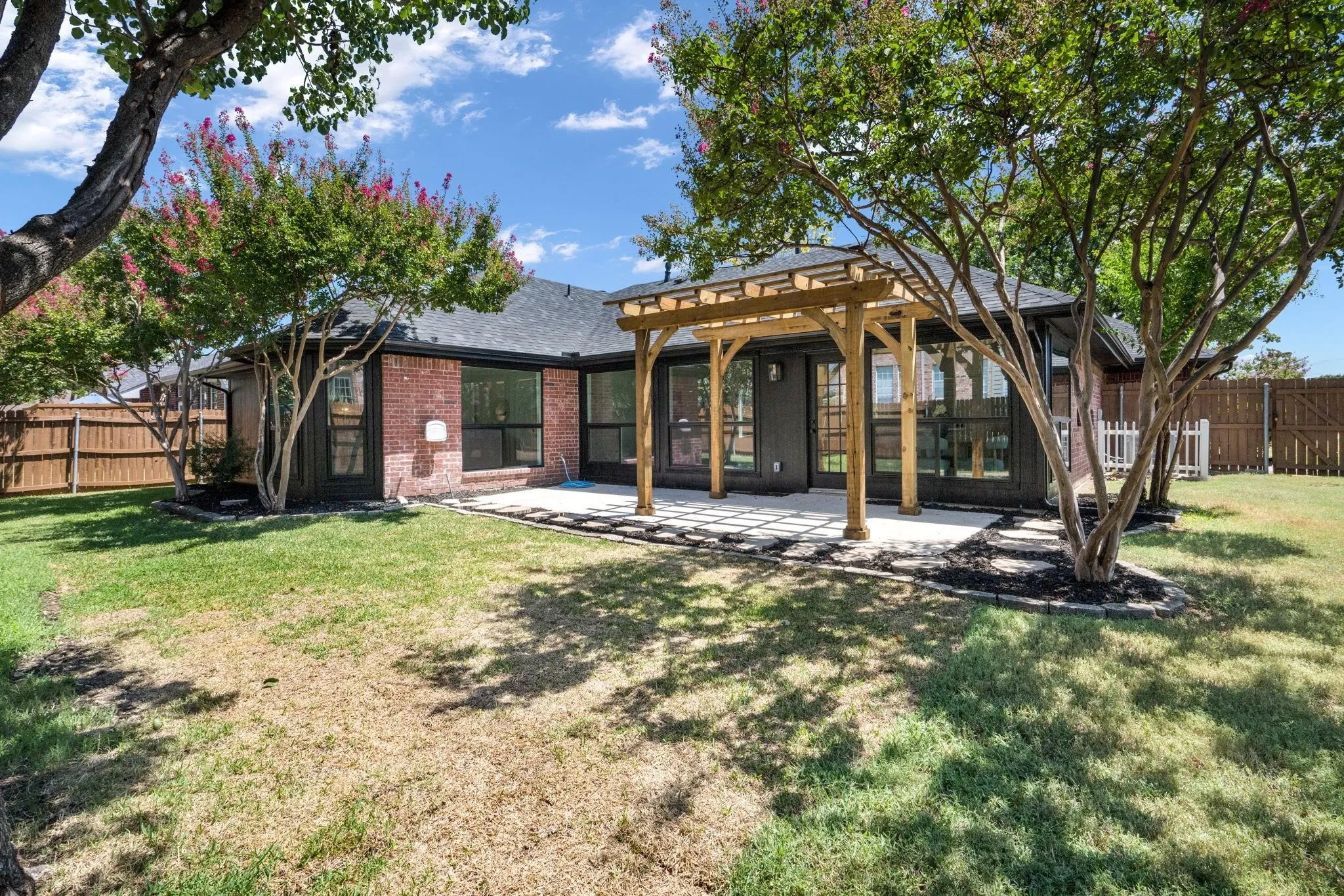 Expansive backyard featuring a wood pergola, stone patio, mature trees, and a brick exterior