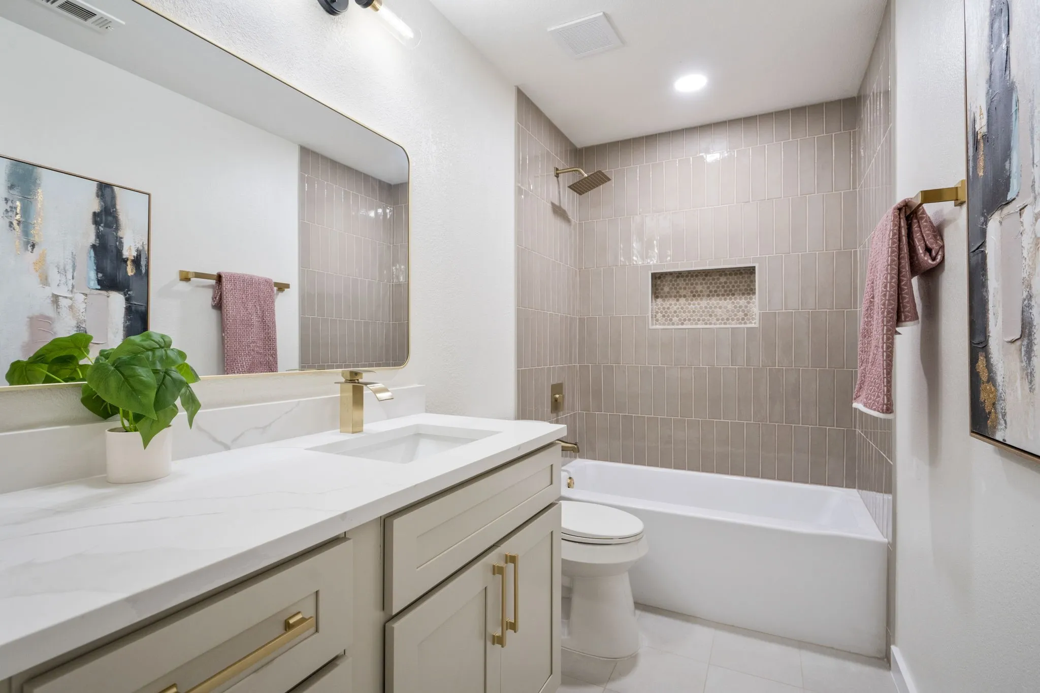 Vanity with an integrated sink and gold-finish faucet, framed mirror, built-in bathtub, and a tiled shower surround with a recessed niche