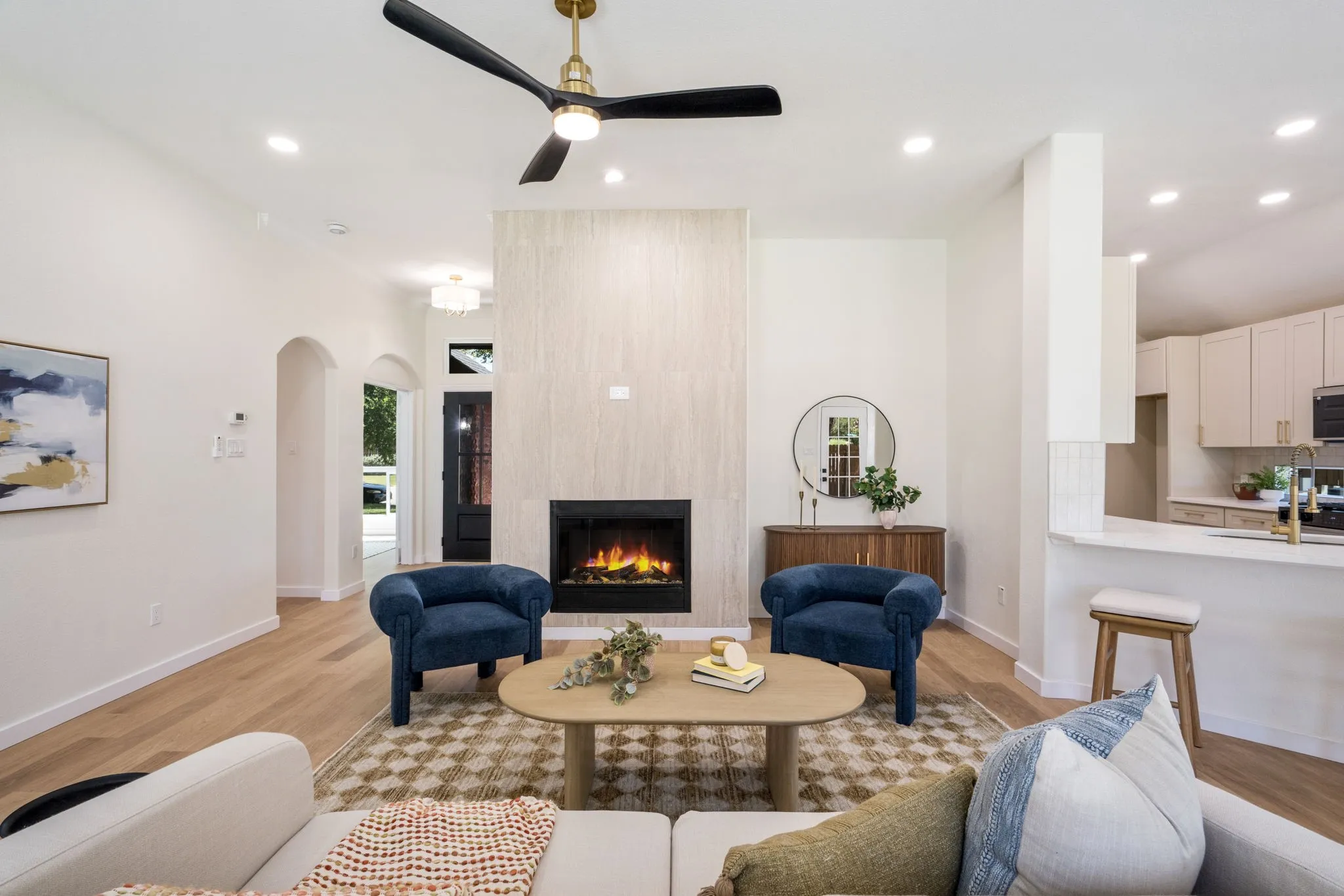 Recessed lighting, wood-finish flooring, electric fireplace with textured surround, arched entryway, and an open concept kitchen with breakfast bar