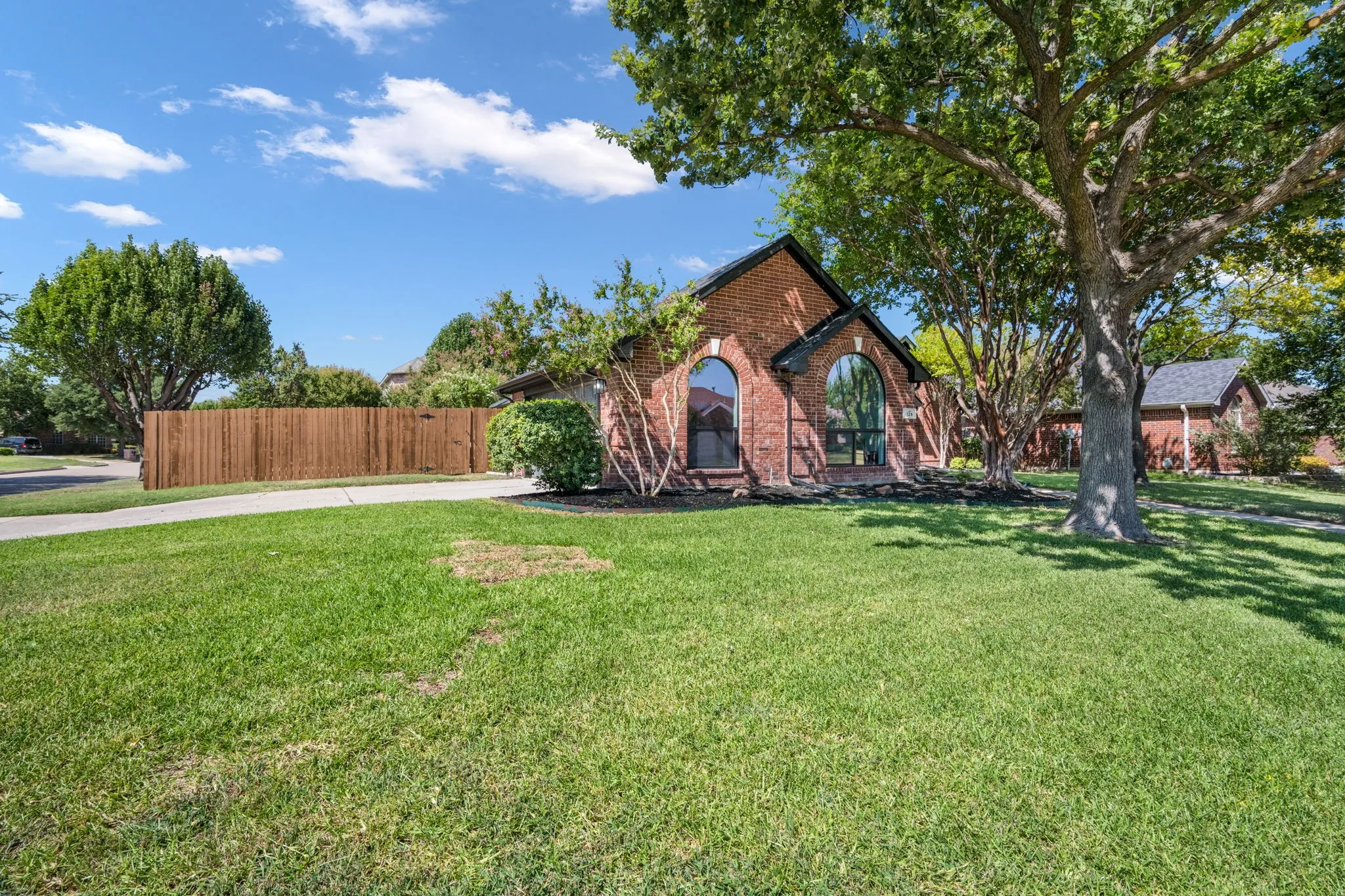 Brick exterior featuring arched windows, mature trees, and a wooden privacy fence