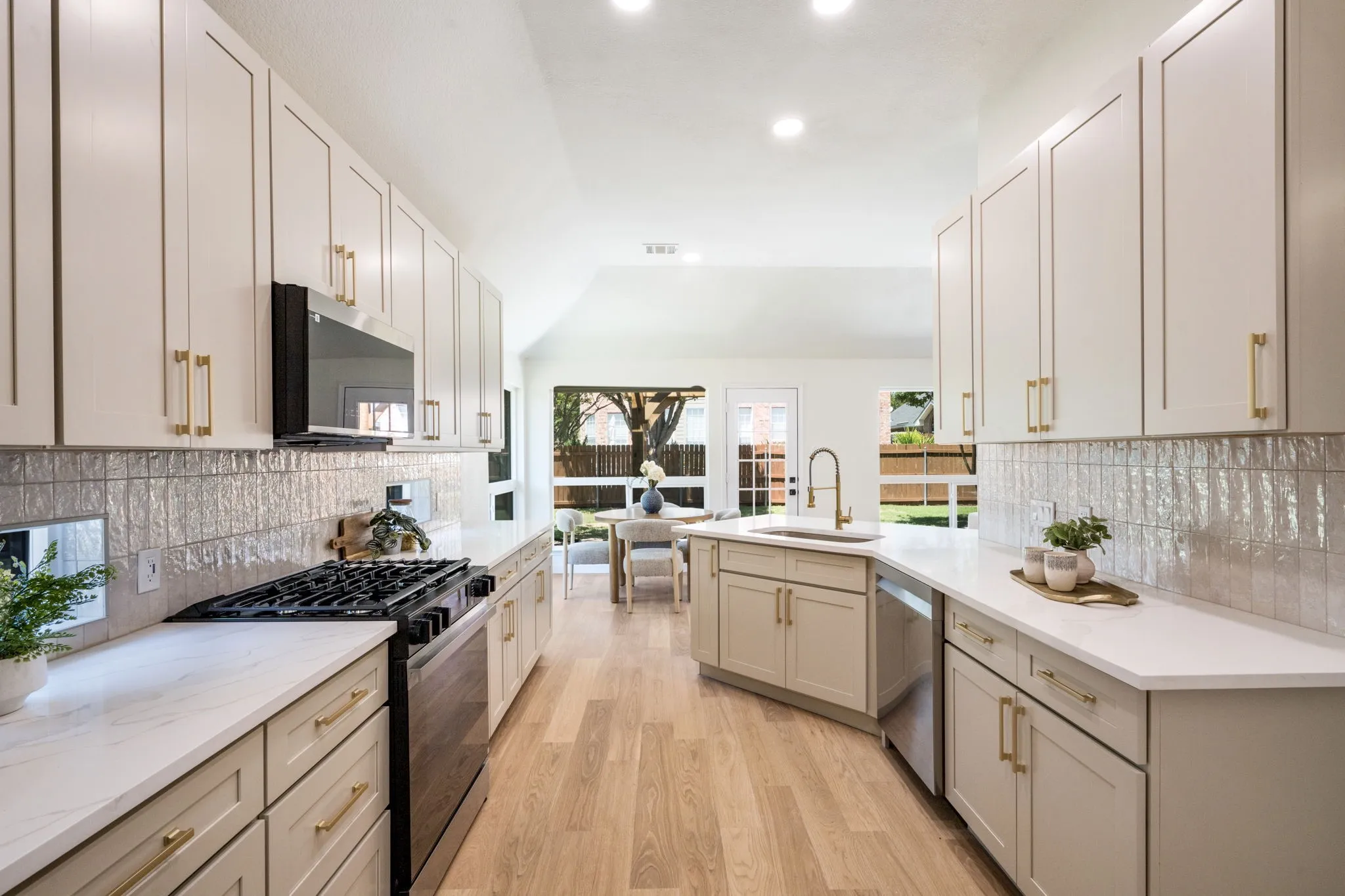 Modern kitchen featuring light-toned cabinetry, a gas range, integrated microwave, wood-finish flooring, and a large window overlooking the exterior