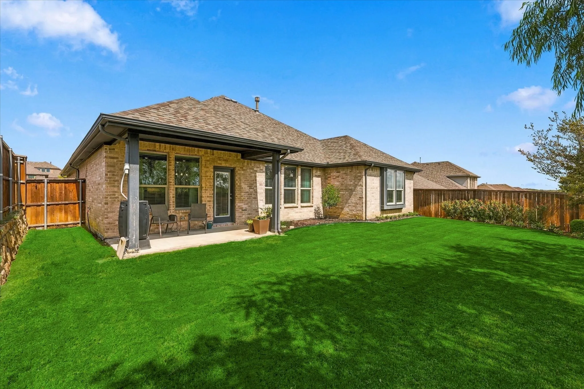 The backyard showcases the home’s attractive brick exterior, covered patio and generous green space—perfect for enjoying outdoor living year-round.