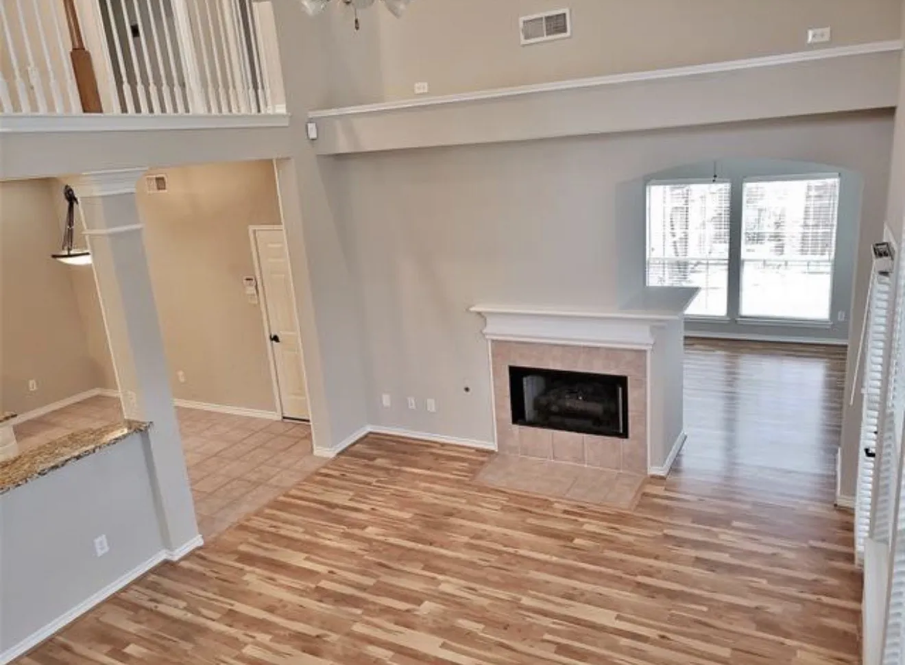 Vaulted ceiling, wood-finish flooring, fireplace with tile surround, arched window, and a white baluster railing