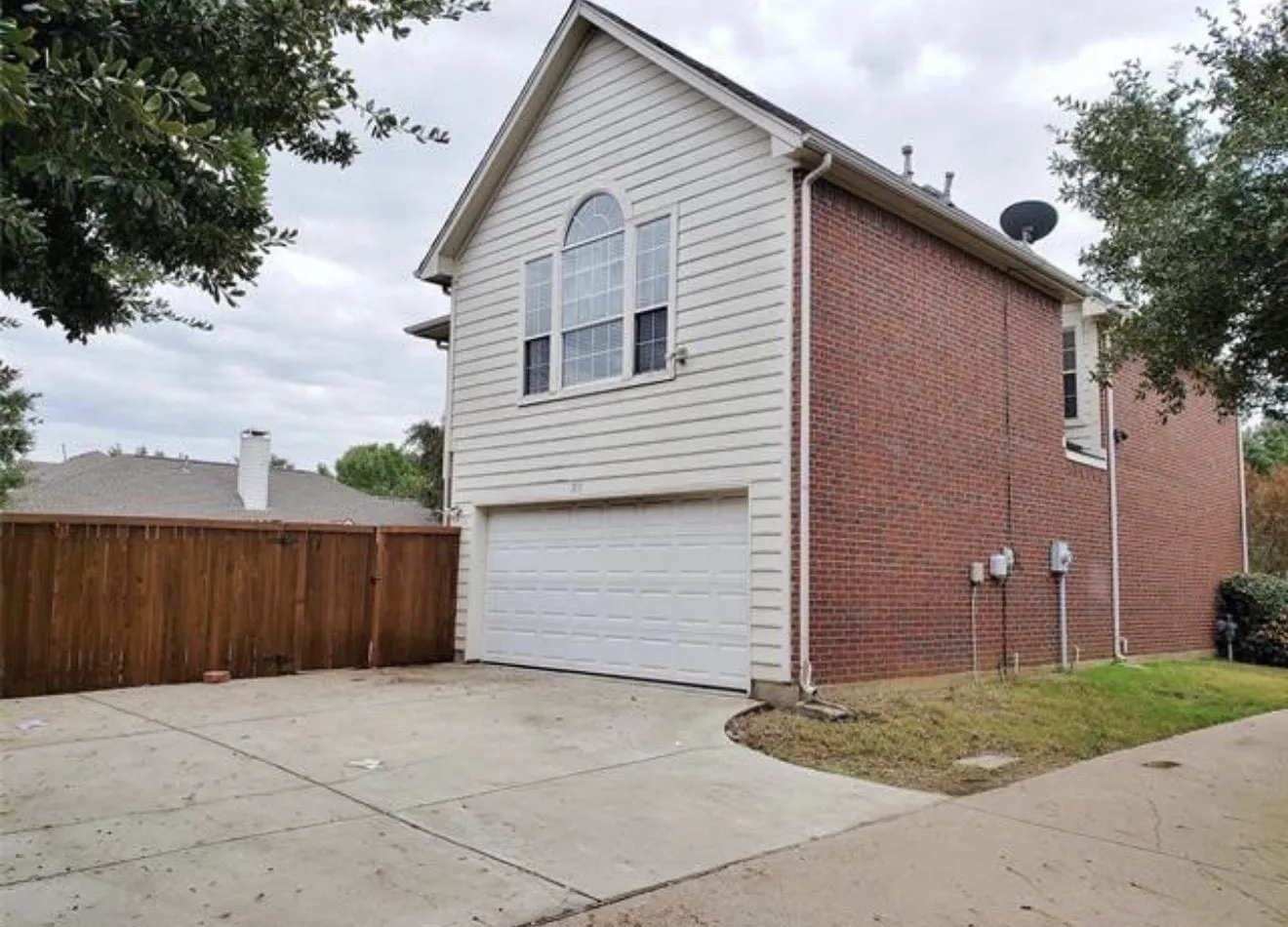 Brick and siding exterior with a prominent arched window, attached garage, and concrete driveway