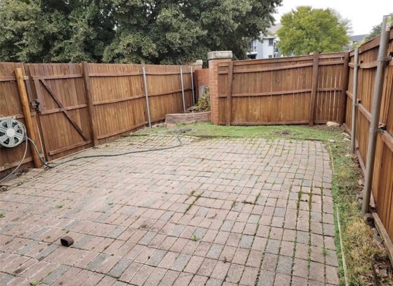 Enclosed outdoor space featuring wood fencing and a brick paver patio