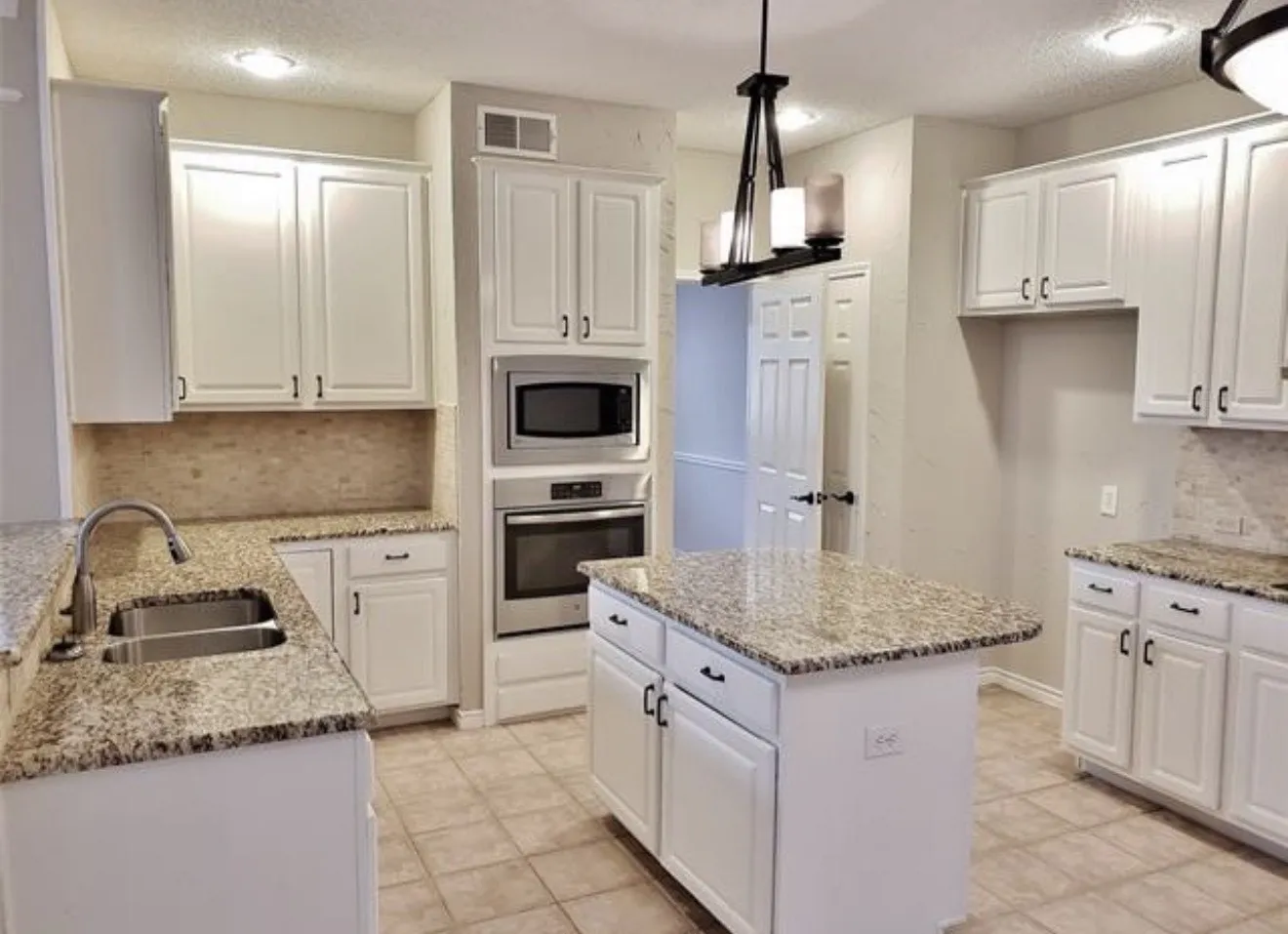 Kitchen featuring white cabinetry, granite countertops, tile backsplash, stainless steel built-in appliances, and a kitchen island with additional storage
