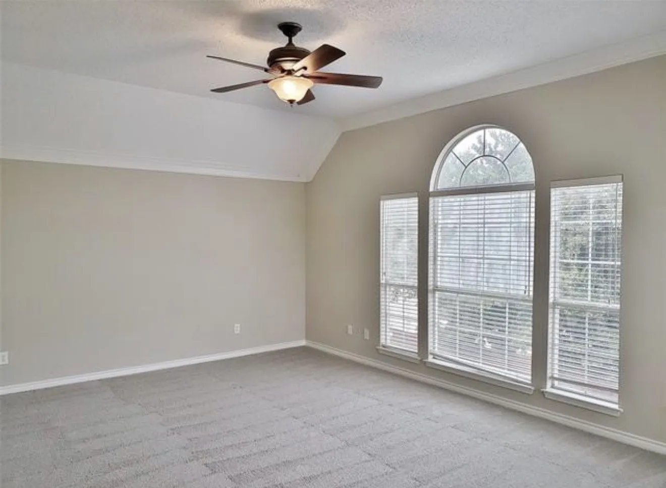 Vaulted ceiling with crown molding, ceiling fan with integrated lighting, and arched window with blinds