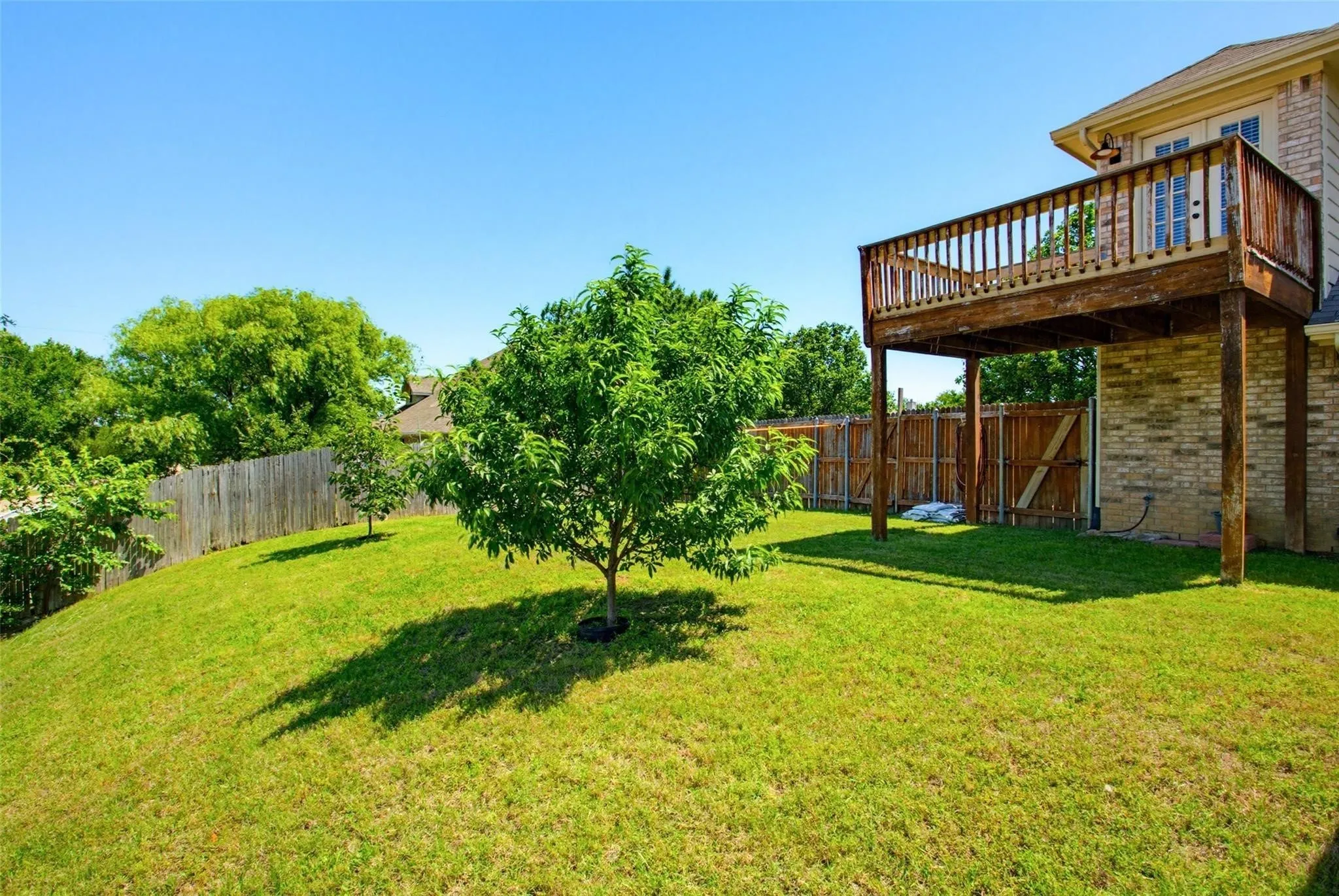 Expansive backyard featuring a manicured lawn, established trees, and a raised wood deck