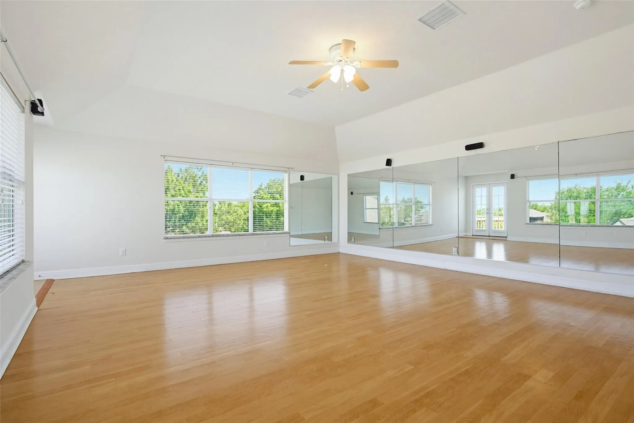 Vaulted ceiling with a ceiling fan, light wood-finish flooring, full-wall mirrors, and multiple windows