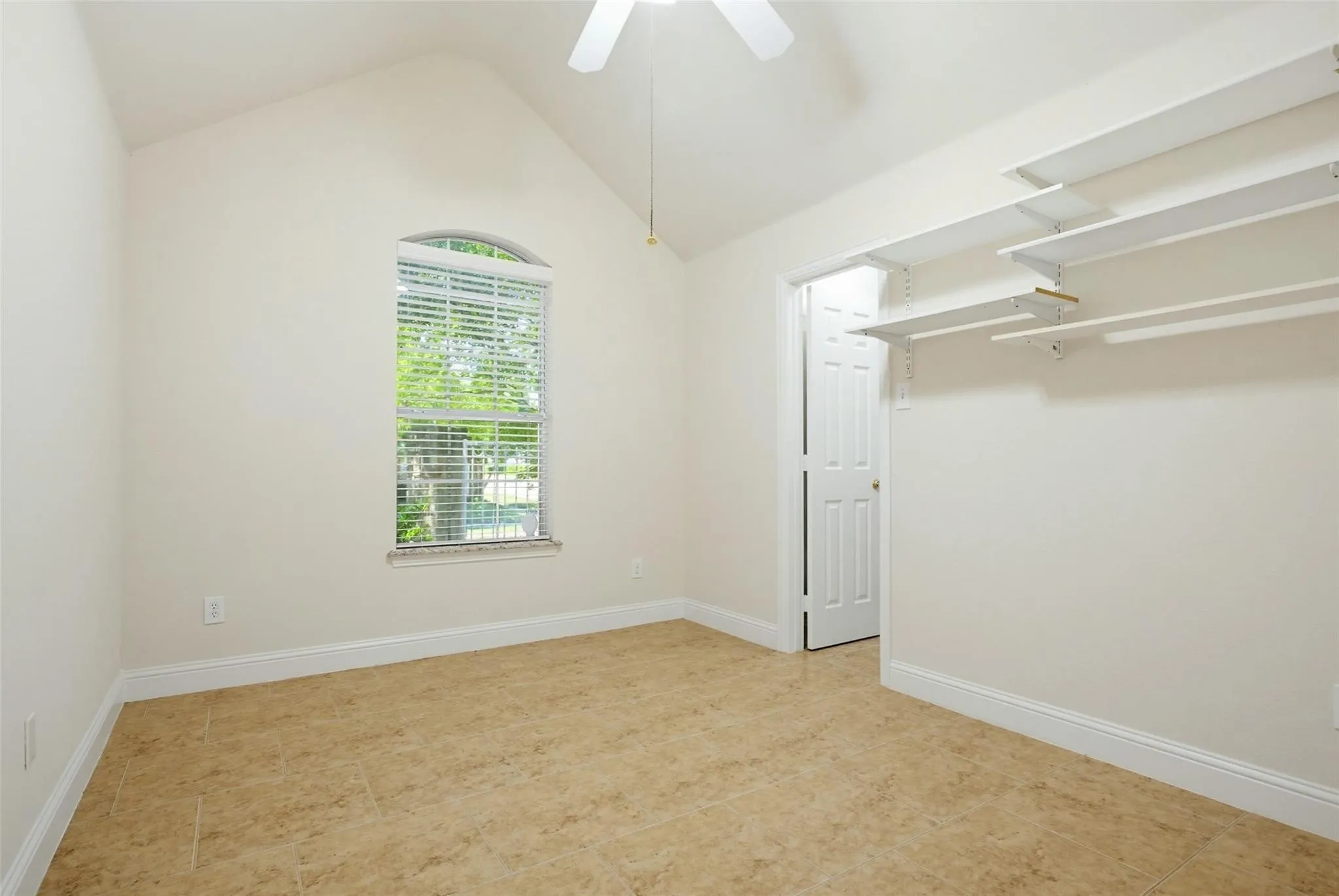 Vaulted ceiling, arched window, tile flooring, ceiling fan, and built-in closet shelving
