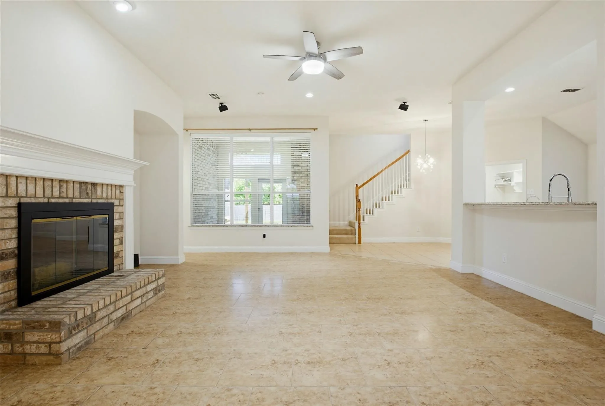 Brick fireplace with a white mantle, large window, tile flooring, and staircase with wood handrails