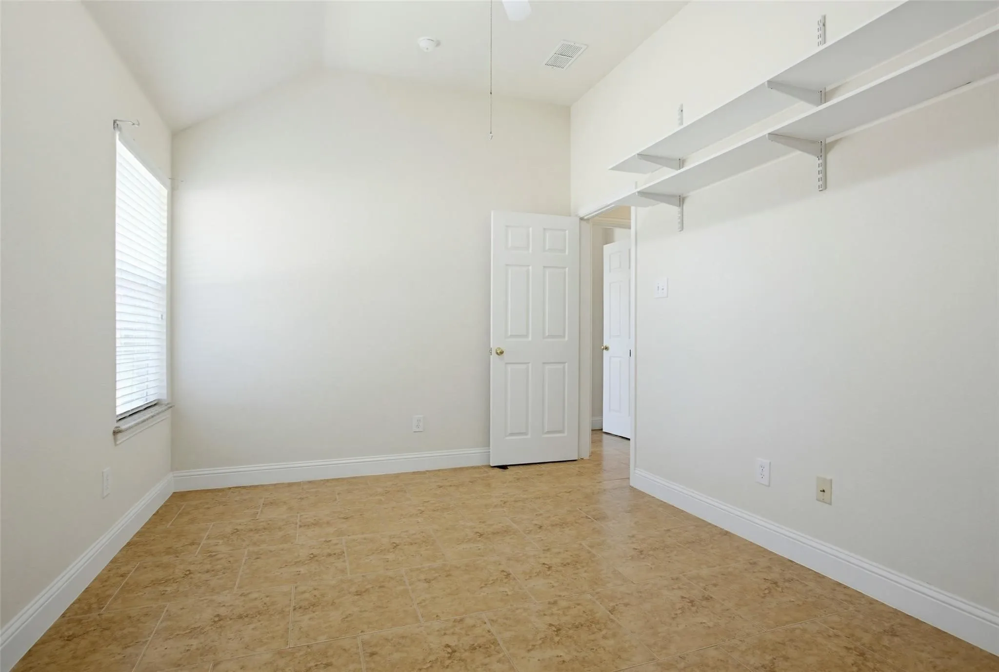 Vaulted ceiling with a ceiling fan, window with blinds, tile flooring, and built-in shelving