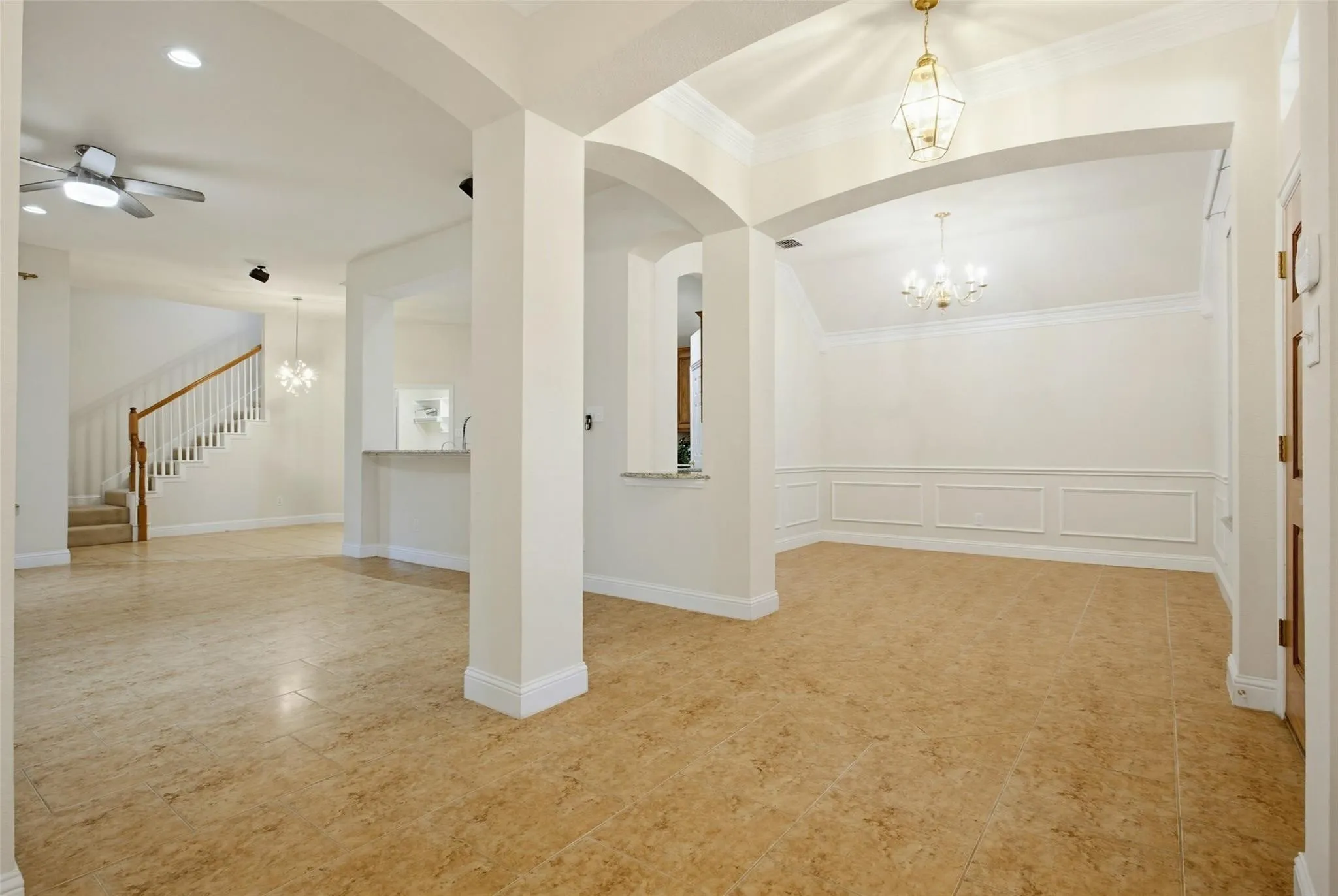 Arched doorways, wainscoting, crown molding, tile flooring, and a chandelier create an elegant interior