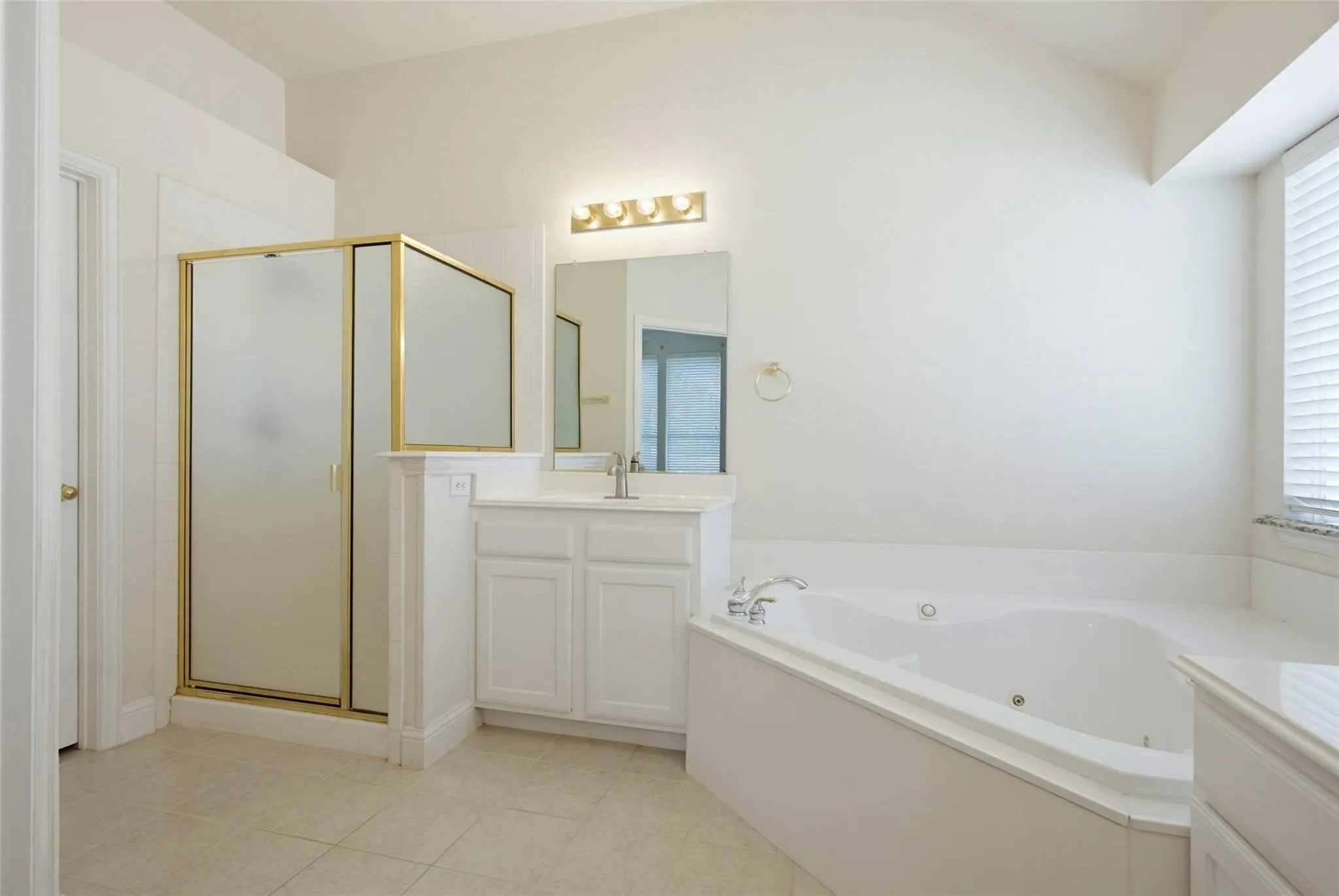 Shower with gold-toned frame, white vanity with integrated sink, corner soaking tub, tile flooring, and vaulted ceiling