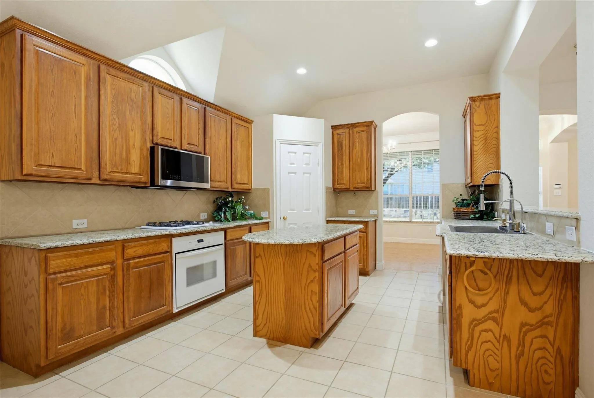 Kitchen featuring wood cabinetry, light-toned countertops, a built-in oven, tile flooring, and an arched entryway