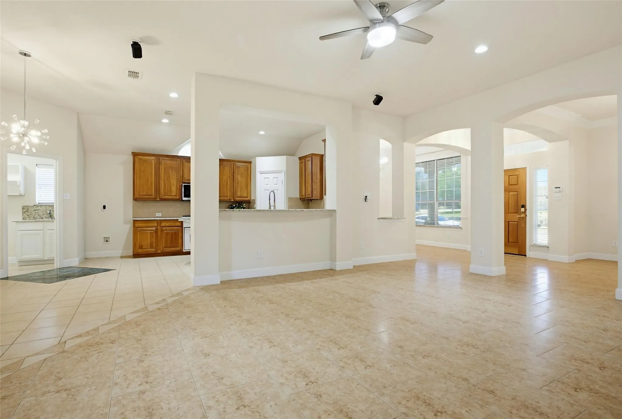 Expansive tiled flooring, arched doorways, a ceiling fan, recessed lighting, and a kitchen featuring wood cabinetry