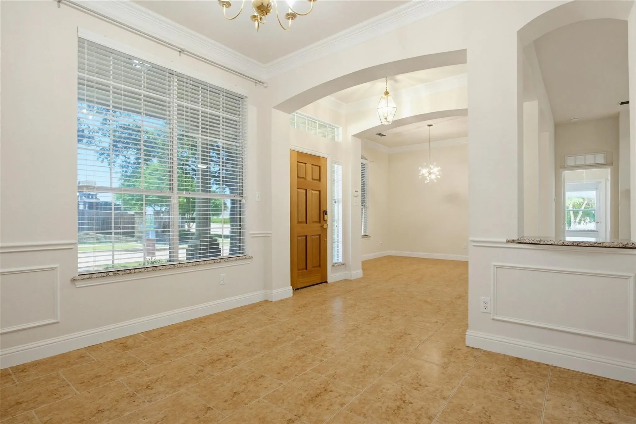 Arched entryways, tile flooring, crown molding, a large front-facing window, and wainscoting details enhance this interior space