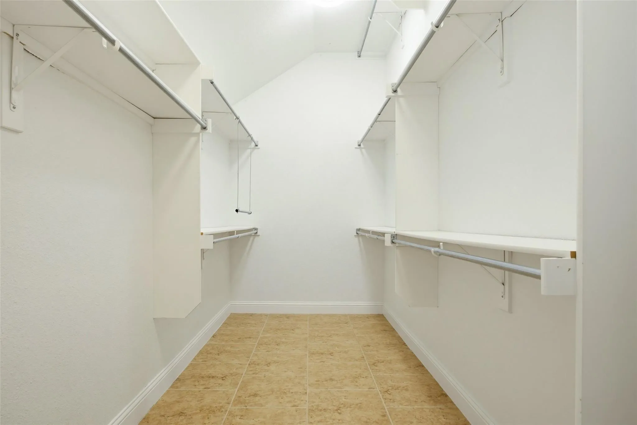 Spacious closet featuring built-in shelving, hanging rods, and tile flooring