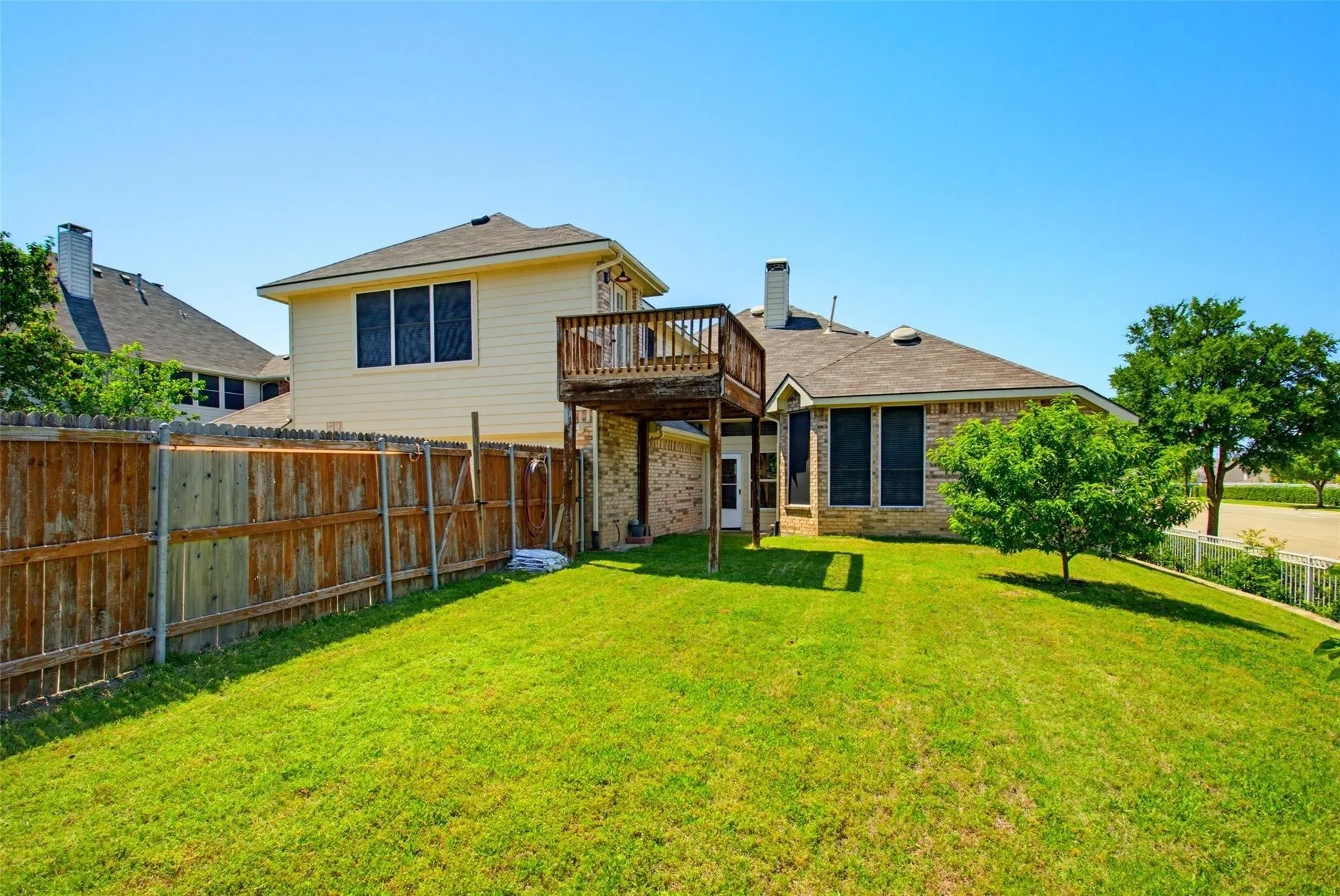 Expansive lawn featuring mature trees, a wooden privacy fence, brick exterior, and an elevated wooden deck