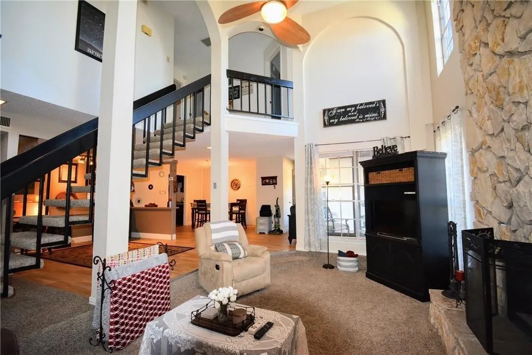 Two-story living area featuring a stone accent wall, high arched ceilings, an open staircase with a balcony, and a ceiling fan