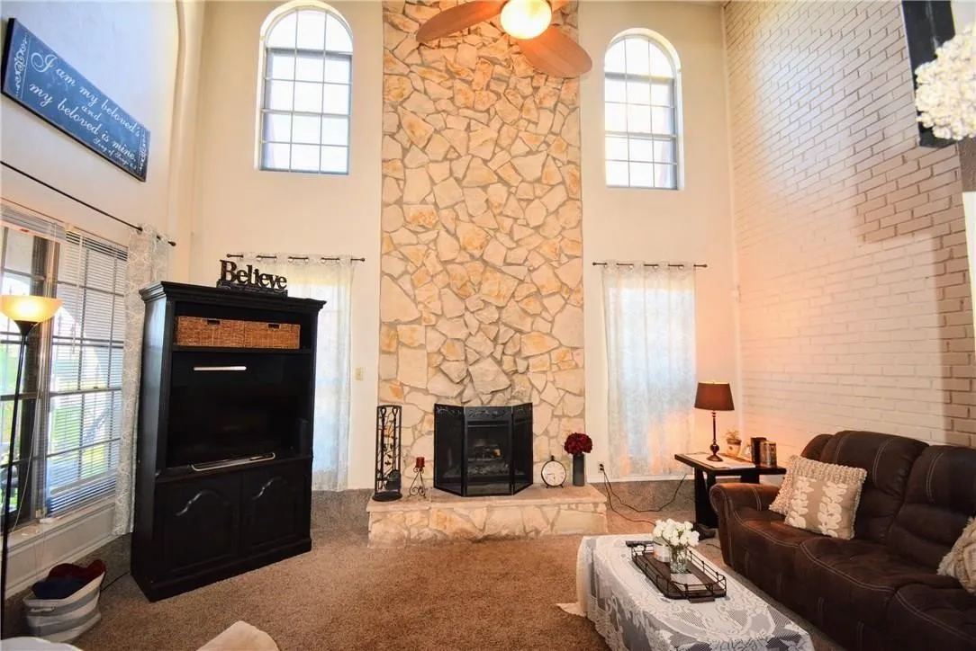 Soaring ceiling with dual arched windows, stone-clad fireplace, and an exposed brick accent wall