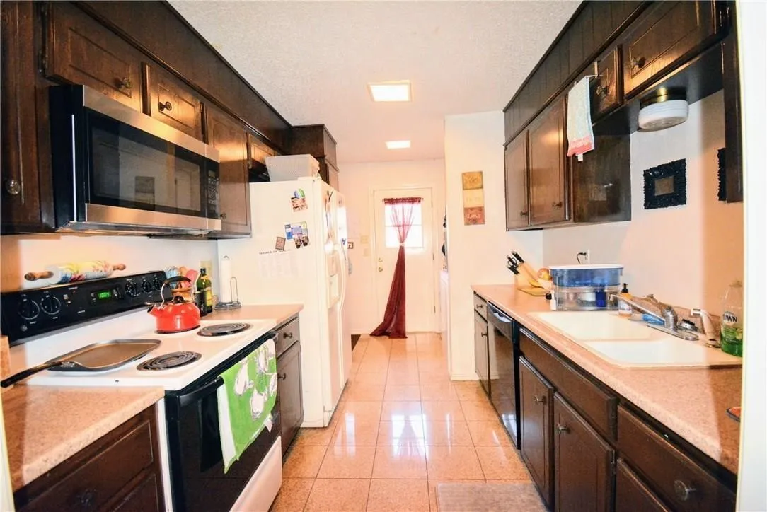Galley kitchen with wood-finish cabinetry, tile flooring, and a stainless steel over-range microwave