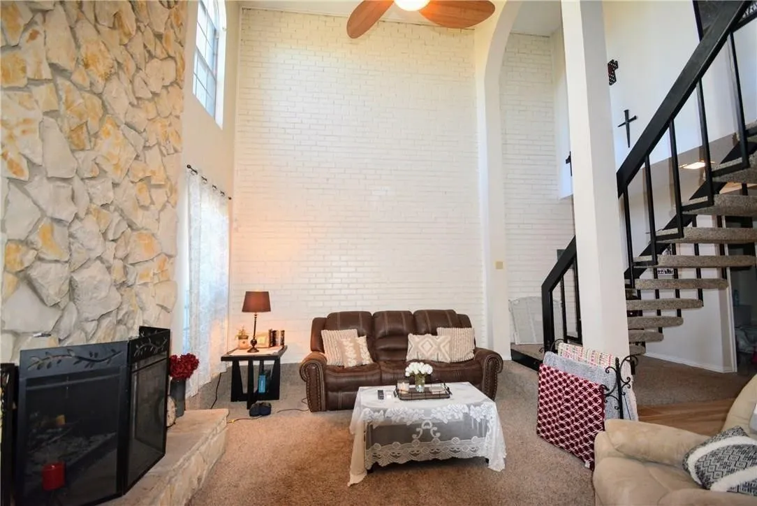 Two-story living area featuring a stone fireplace, high ceilings, a spiral staircase with metal railings, and clerestory windows