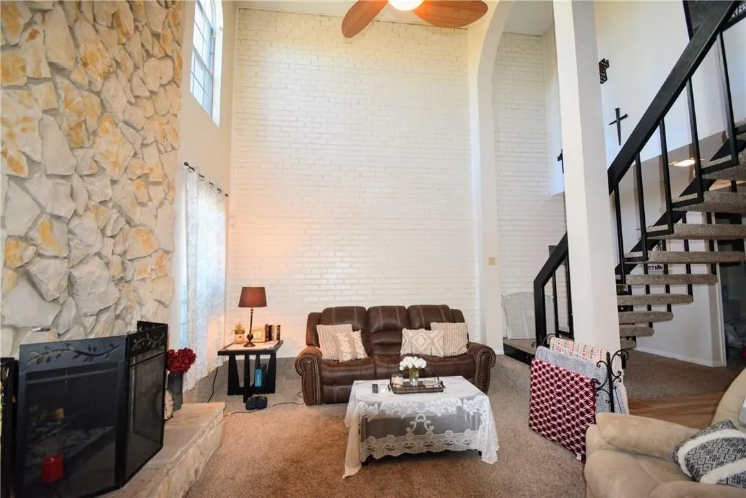 Two-story living area featuring a stone accent wall, fireplace with stone hearth, and a spiral staircase with black metal railings