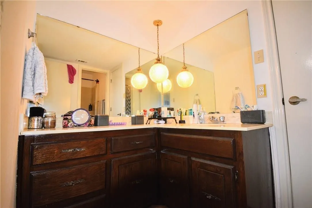 Corner vanity with dark wood-finish cabinetry, light-toned countertop, and expansive wall-mounted mirror