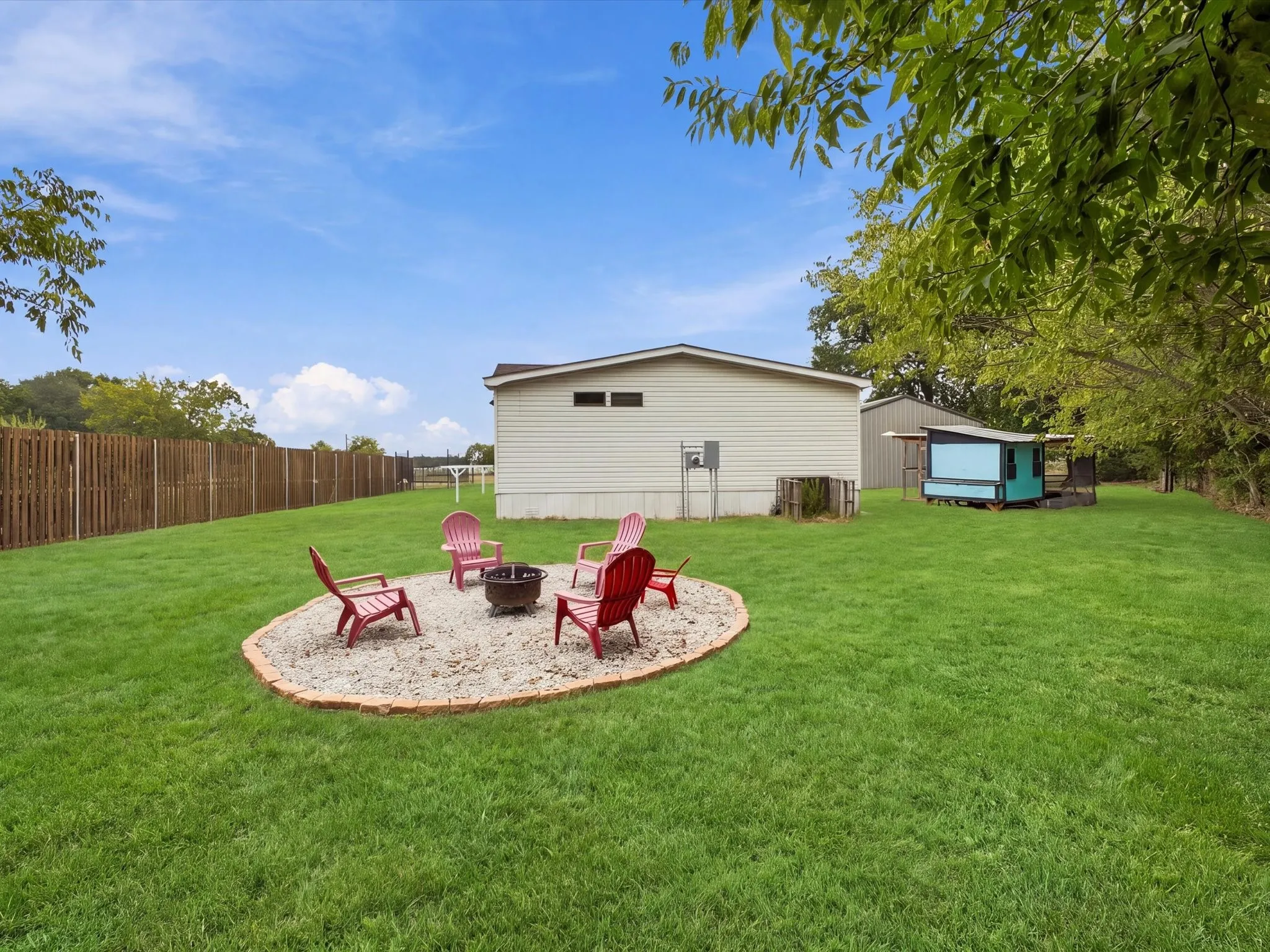 Expansive yard featuring a fire pit area with gravel hardscaping, a privacy fence, and a detached outbuilding