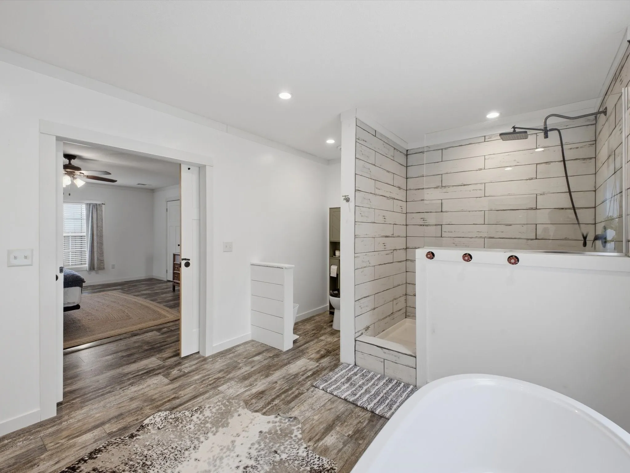 Wood-finish flooring throughout, freestanding soaking tub, and a shower with subway tile surround and dark-finish fixtures