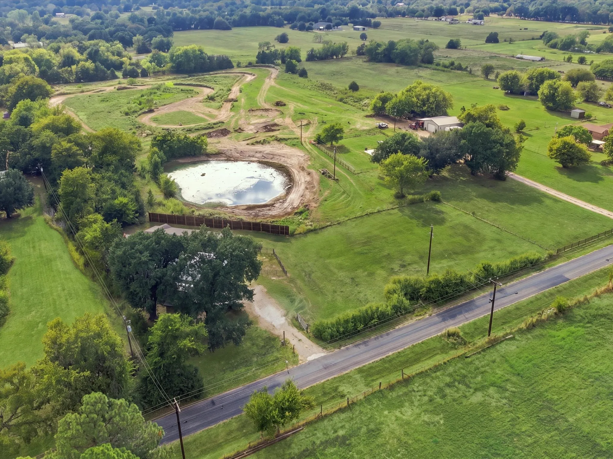 Expansive green acreage featuring a large pond, established trees, and a developed dirt track
