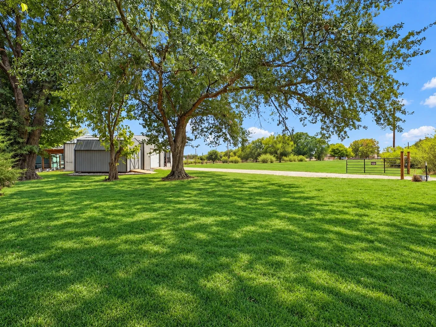 Expansive lawn area with mature trees, a metal-sided outbuilding, and a gated entry