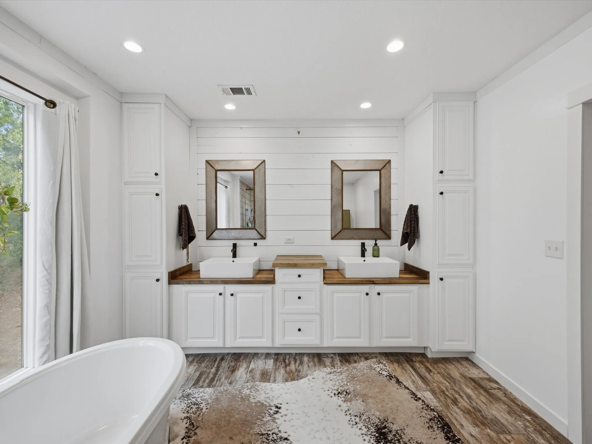 Dual vanity with wood-finish countertops, white shaker cabinetry, and vessel sinks