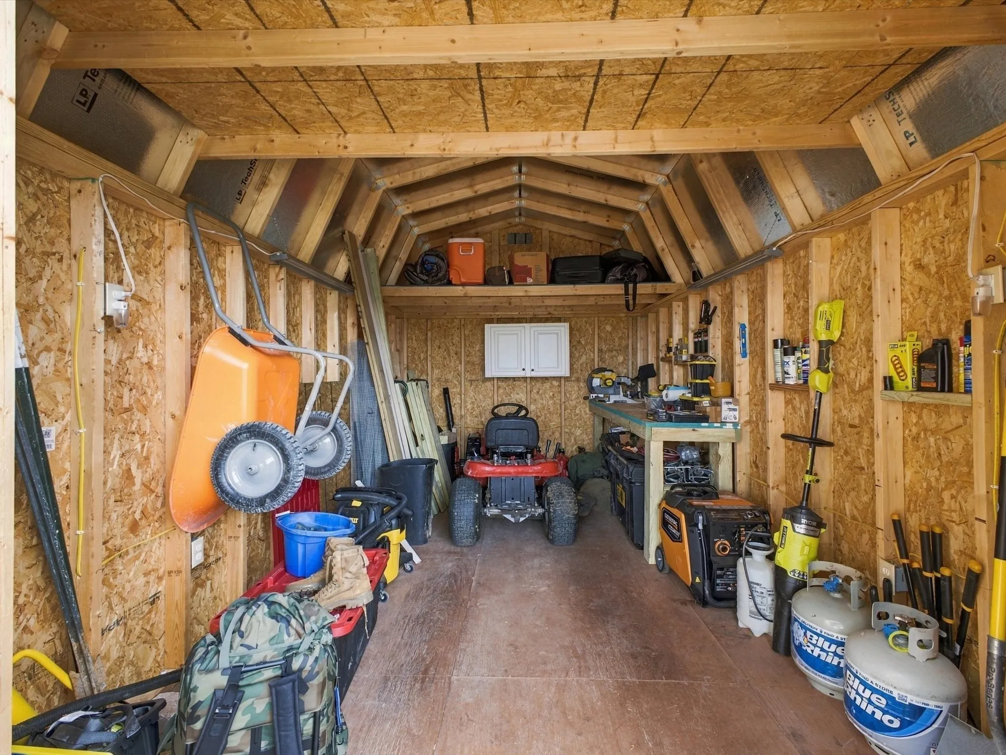 Utility structure featuring wood-finish walls, exposed wood framing, an overhead storage loft, and a built-in workbench