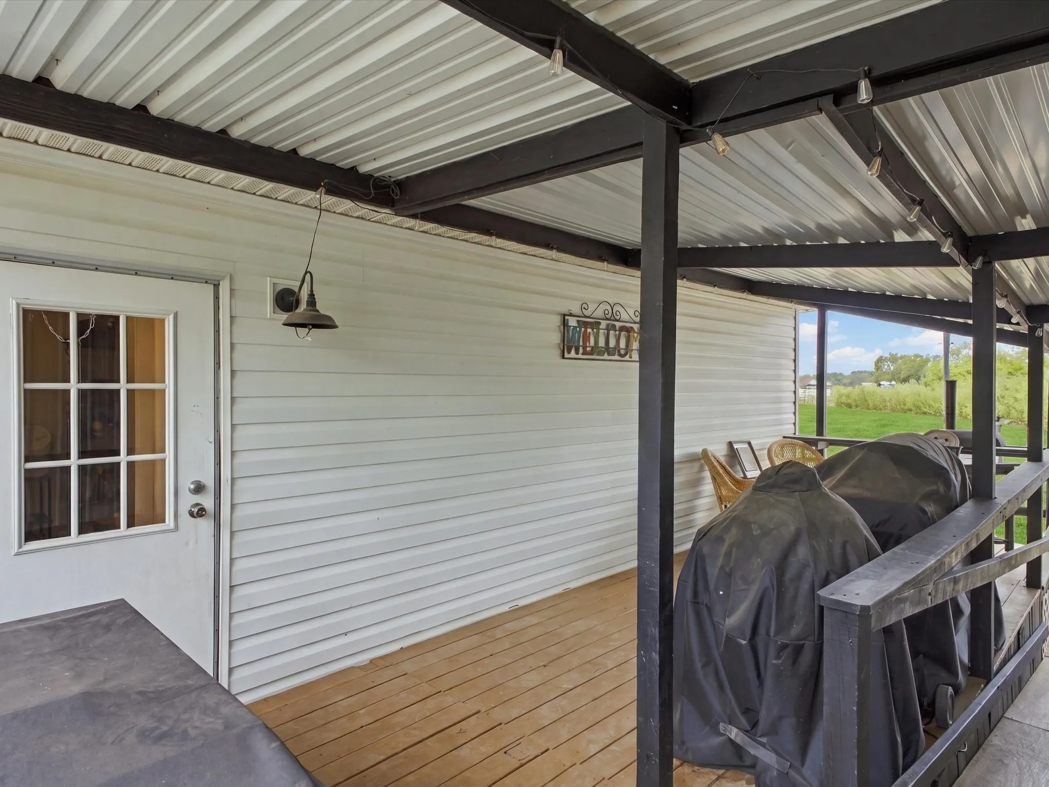 Covered outdoor patio with wood-finish flooring, white siding, and a partial railing