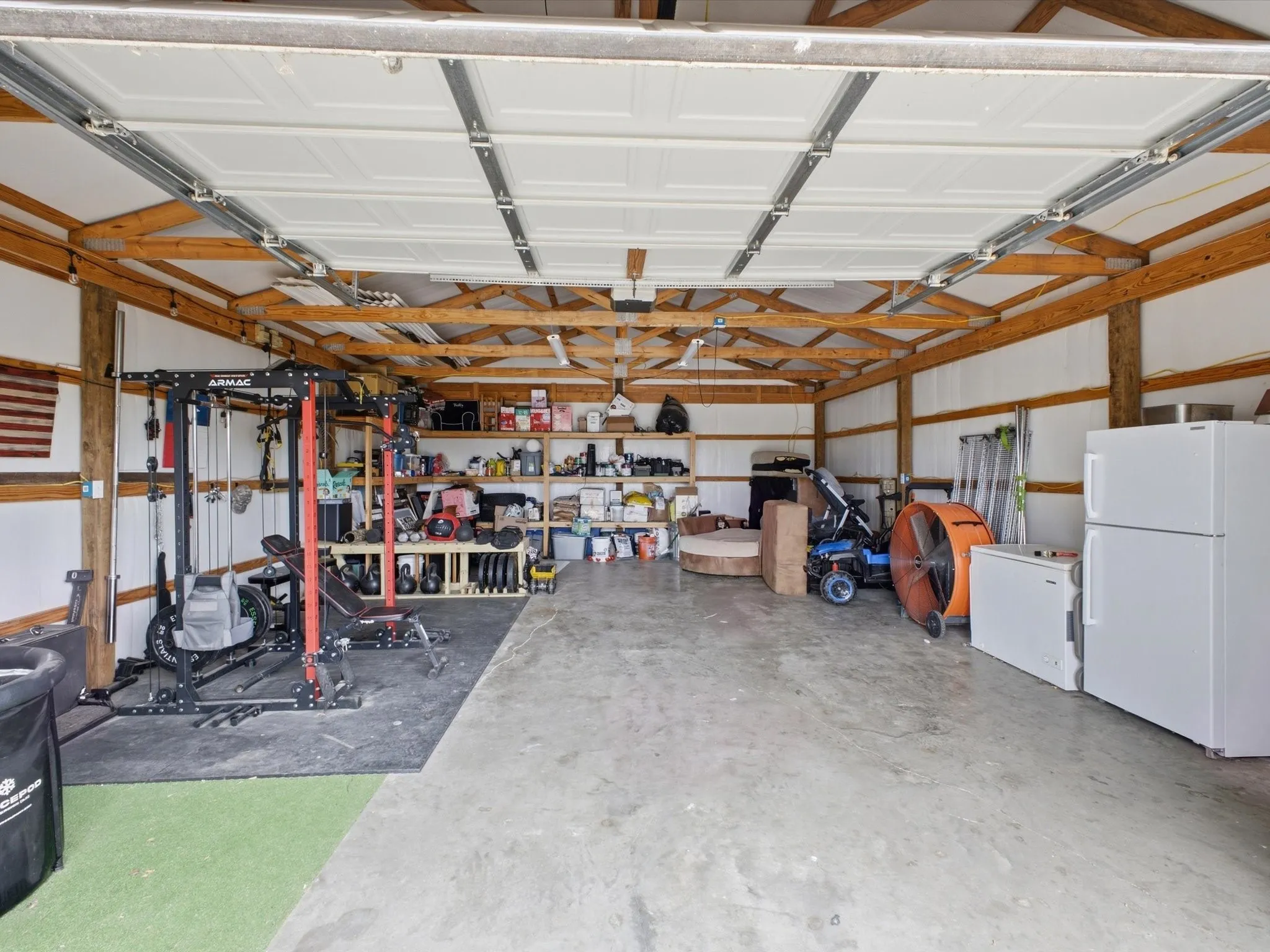 Spacious garage with exposed wood beam ceiling, concrete flooring, and ample built-in shelving