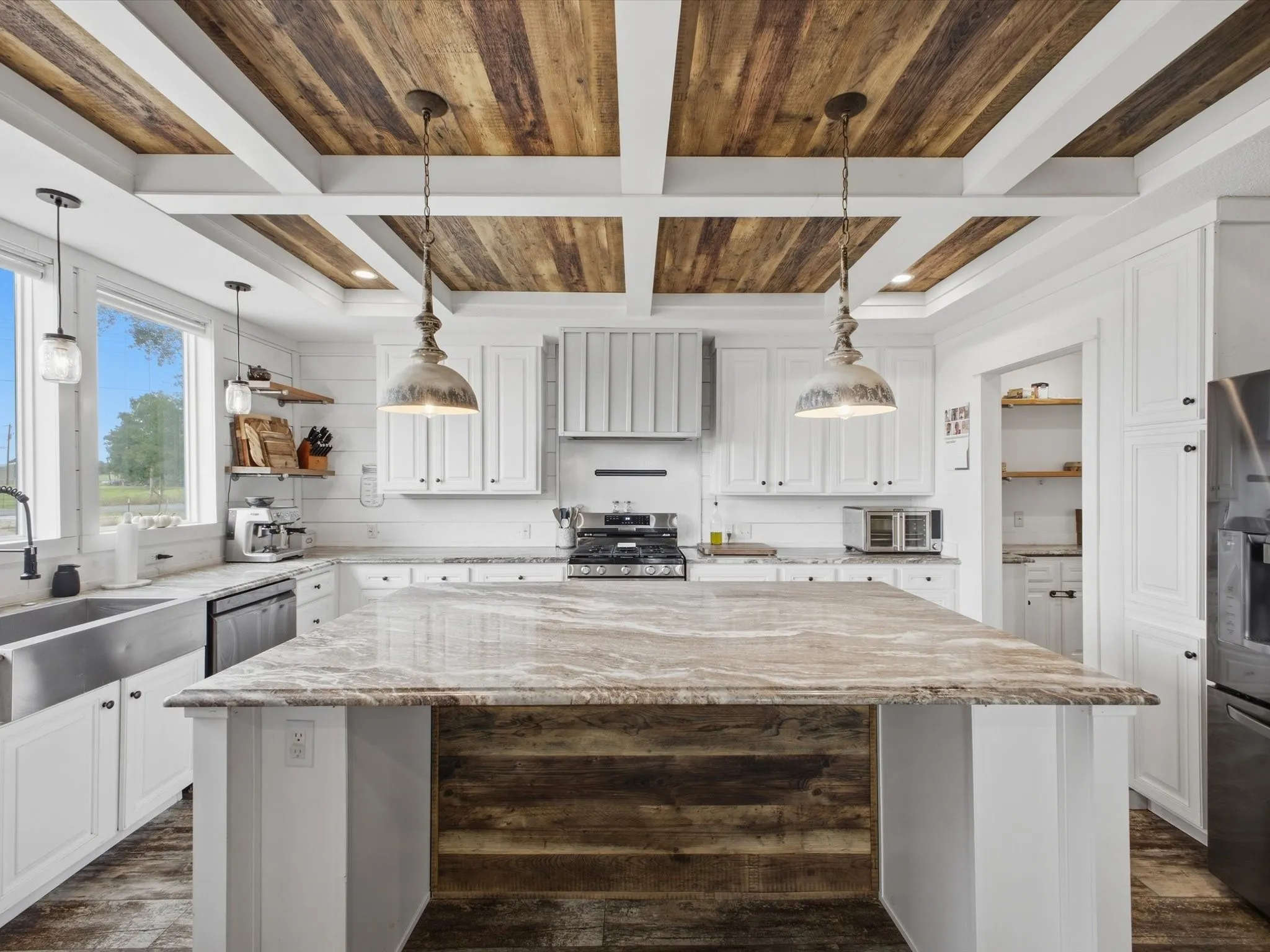 Kitchen featuring a wood-panel ceiling with white beams, a substantial center island with a stone countertop, white cabinetry, a stainless steel sink, and wood-finish flooring