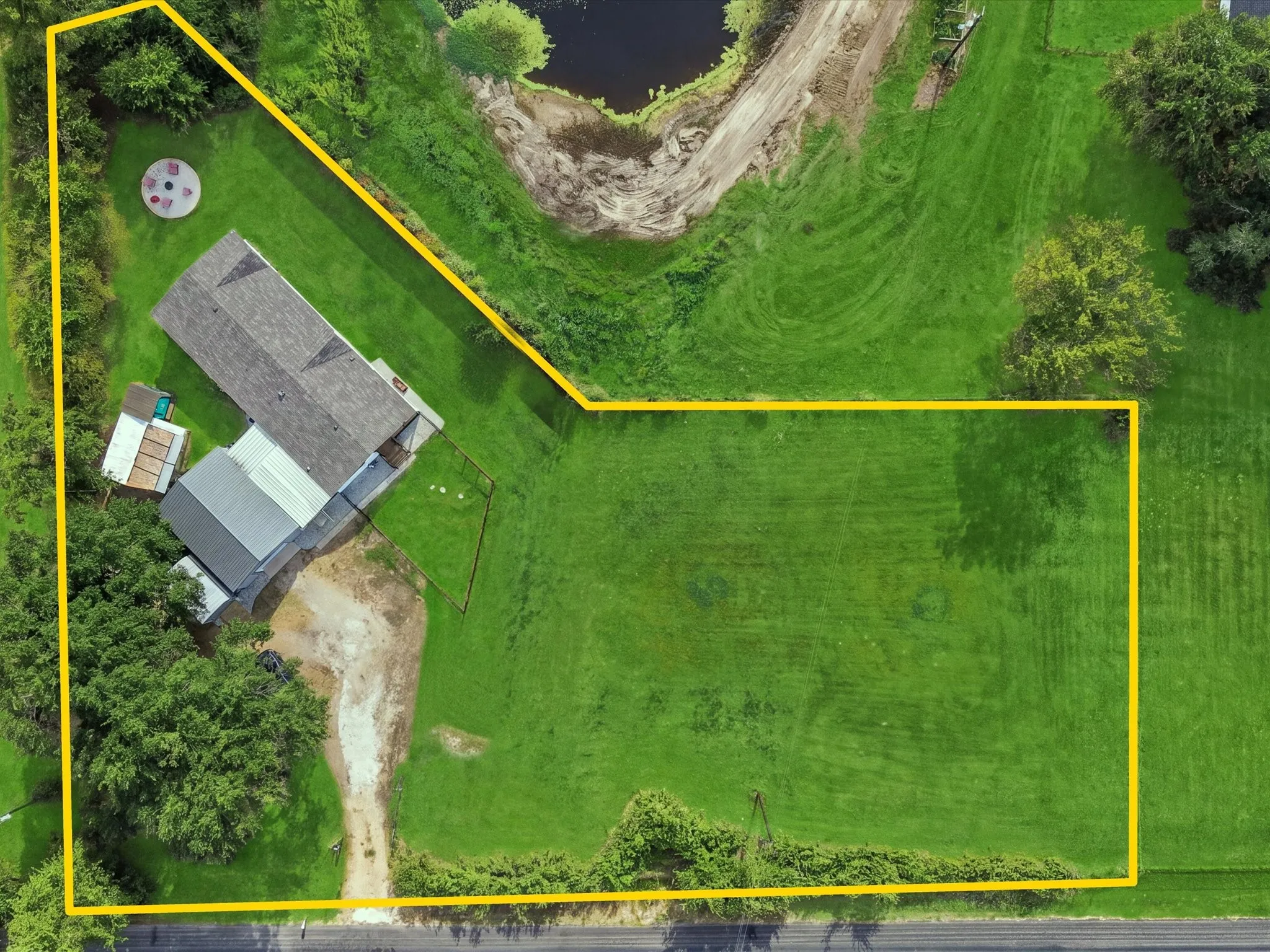 Expansive grassy lot featuring a pond, mature trees, and a gravel driveway