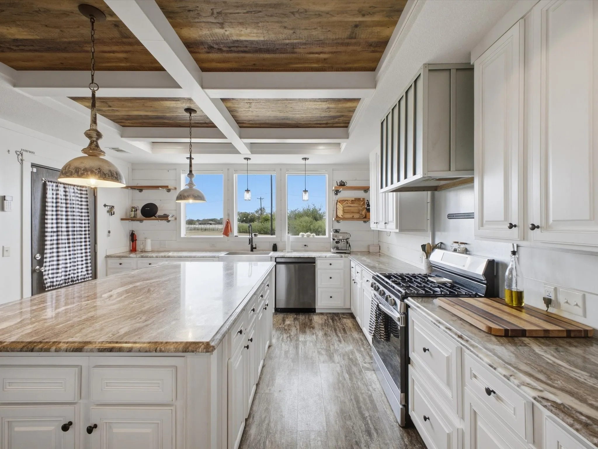 Kitchen featuring a large island with a stone-finish countertop, white cabinetry, stainless steel appliances, and a wood-paneled coffered ceiling
