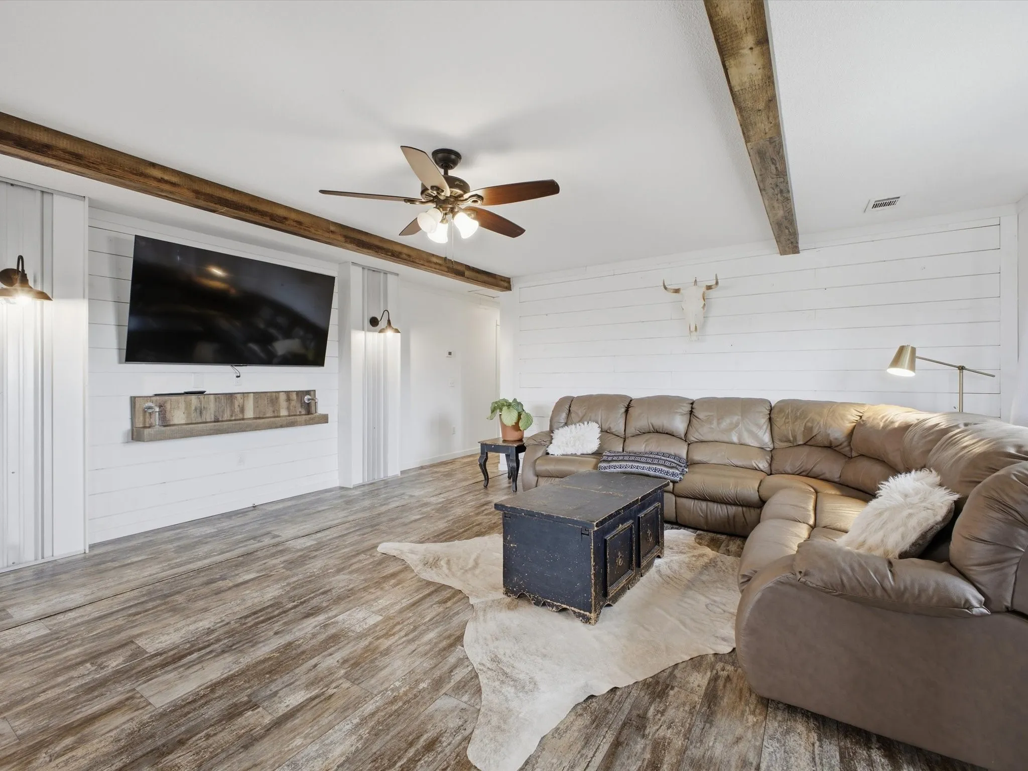 Wood-finish flooring, white shiplap walls, exposed wood beams, and a ceiling fan with integrated lighting