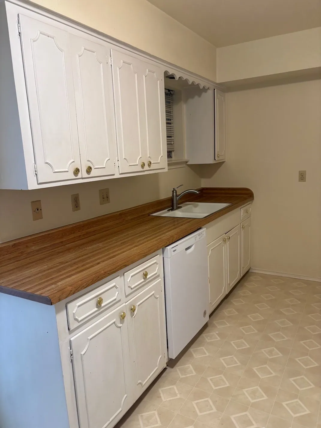 White cabinetry with gold-tone hardware, wood-finish countertops, undermount sink with a stainless-steel faucet, and a white dishwasher