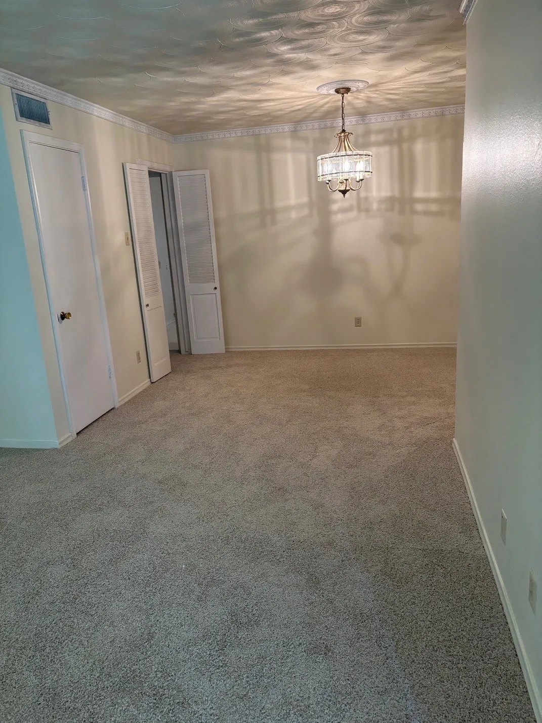 Wall-to-wall carpeting with a decorative ceiling fixture, crown molding, and bifold closet doors