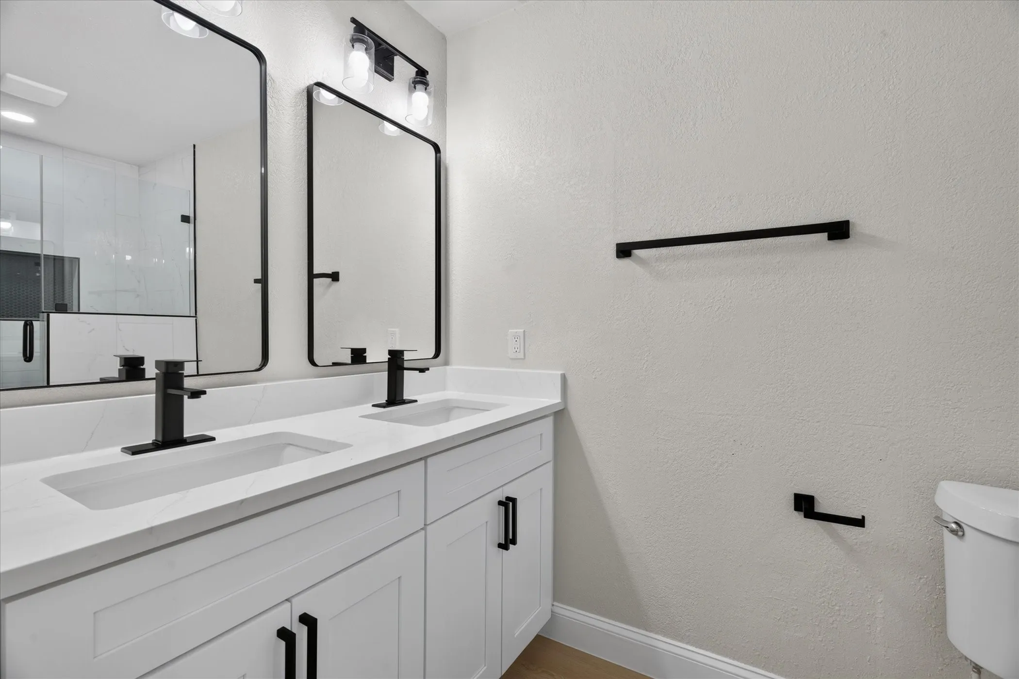 Dual vanity with white shaker cabinetry, white countertop, and matte black fixtures