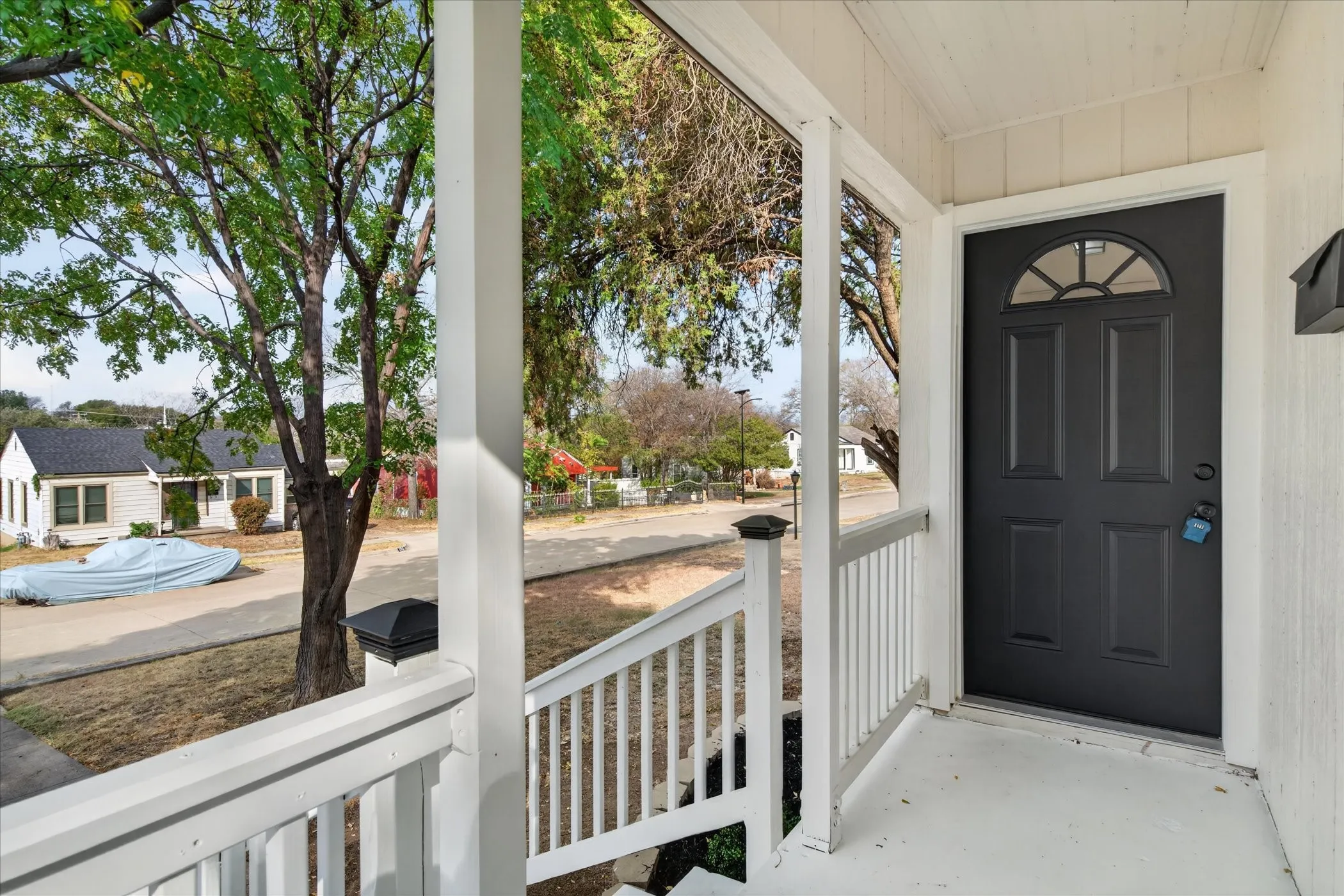 Covered front porch with white railings, a dark paneled entry door, and a decorative transom window