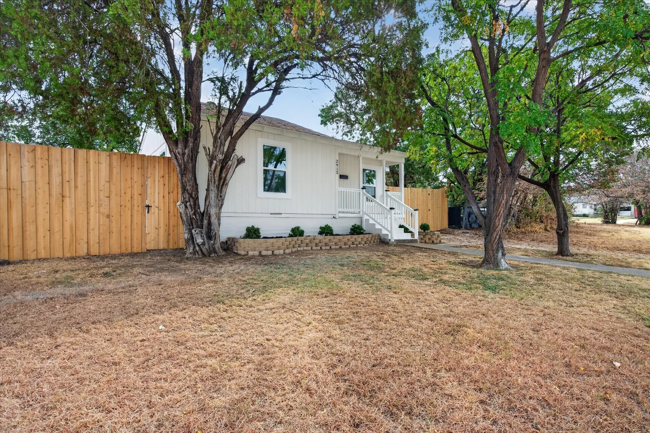 Exterior featuring white siding, a covered porch with white railings, and a wood privacy fence