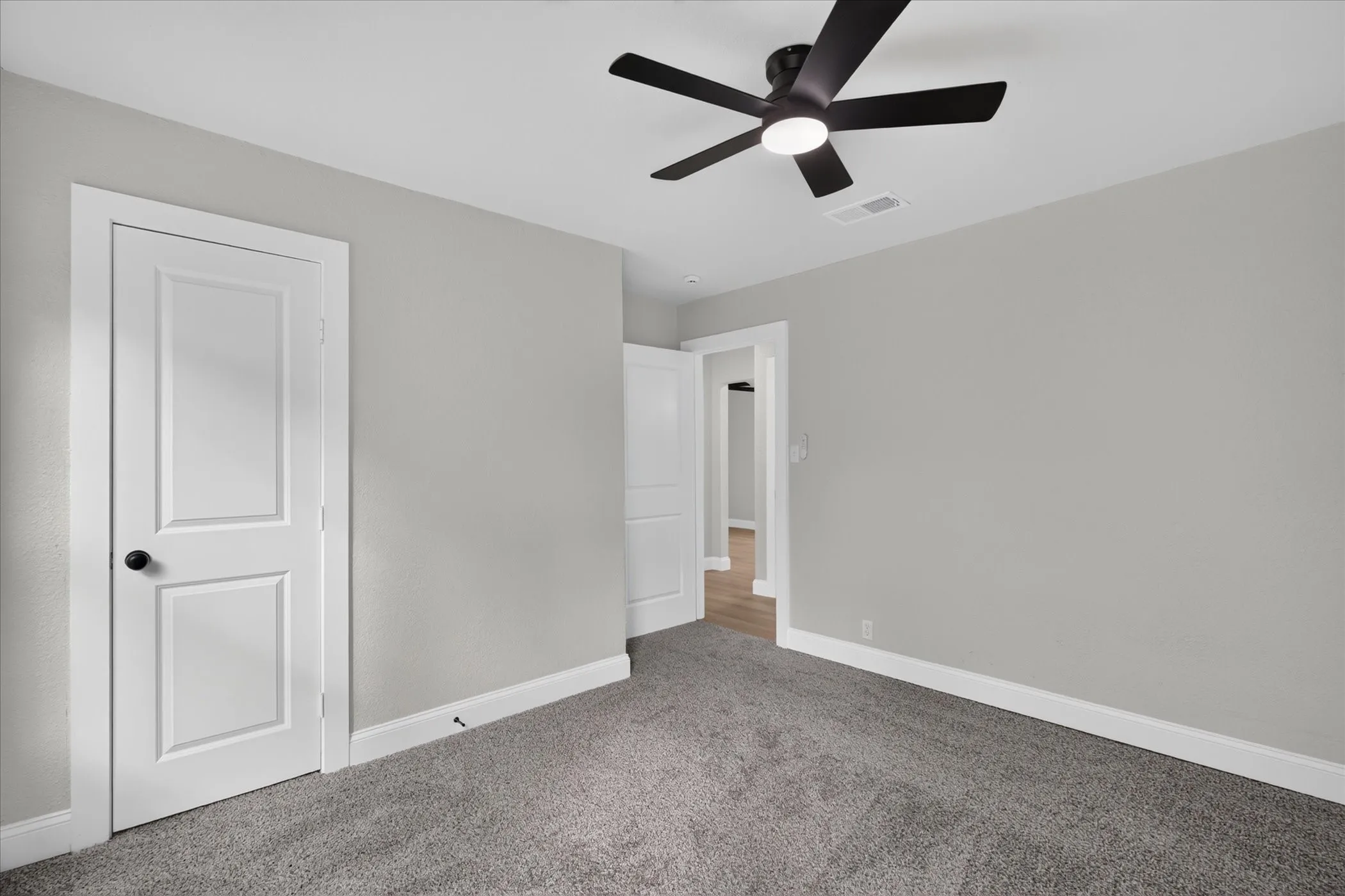 Light gray wall paint, gray carpet flooring, contemporary ceiling fan with integrated lighting, white interior doors, and white trim