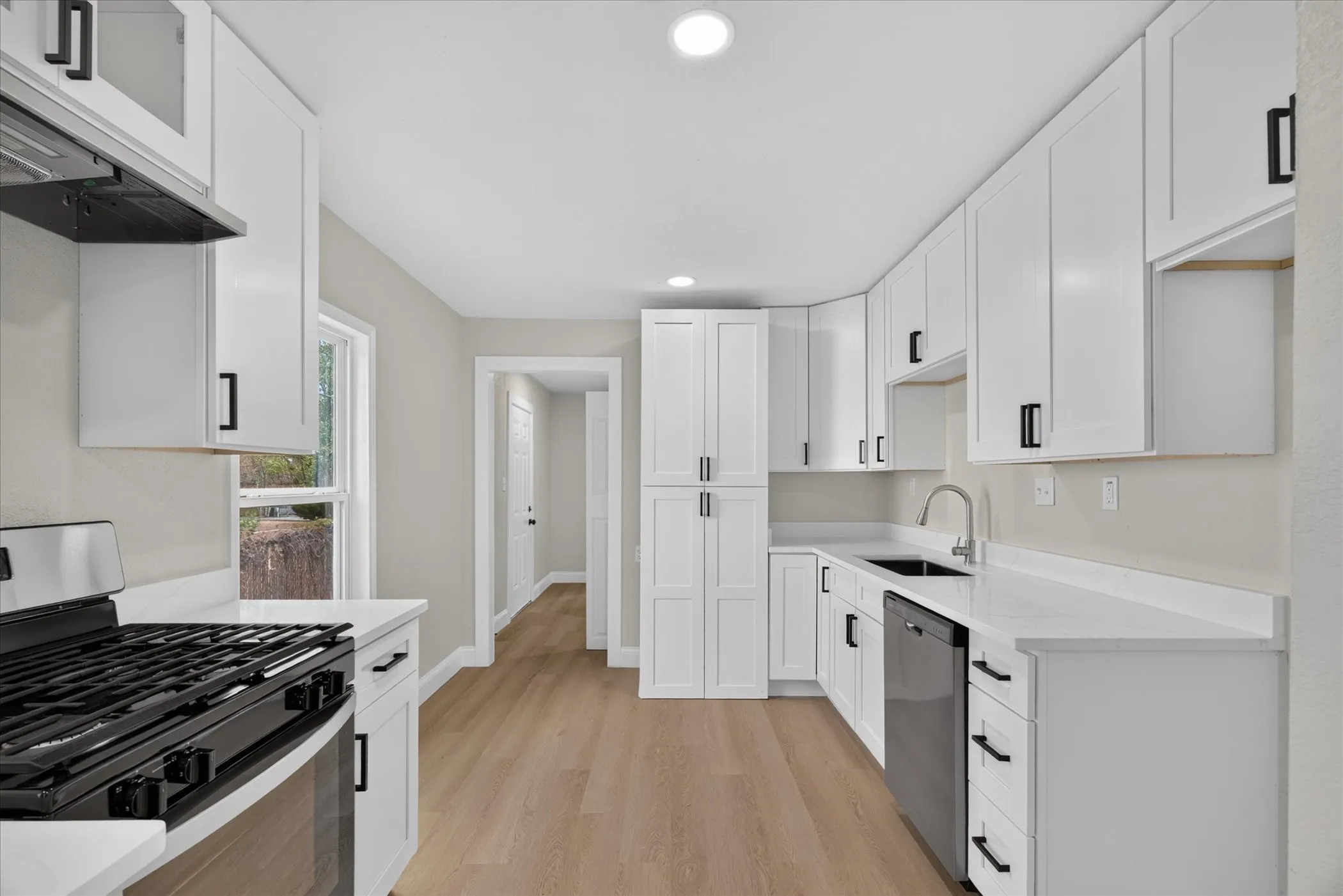 Updated kitchen featuring white shaker cabinetry, white countertops, stainless steel appliances, and wood-finish flooring