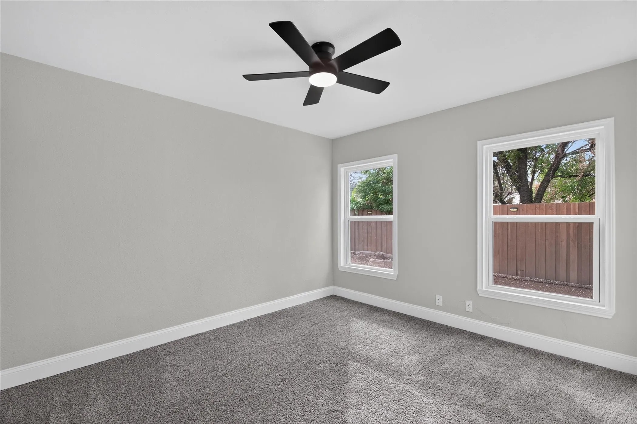 Recessed lighting, ceiling fan, two windows with white trim, light gray walls, and gray carpet flooring